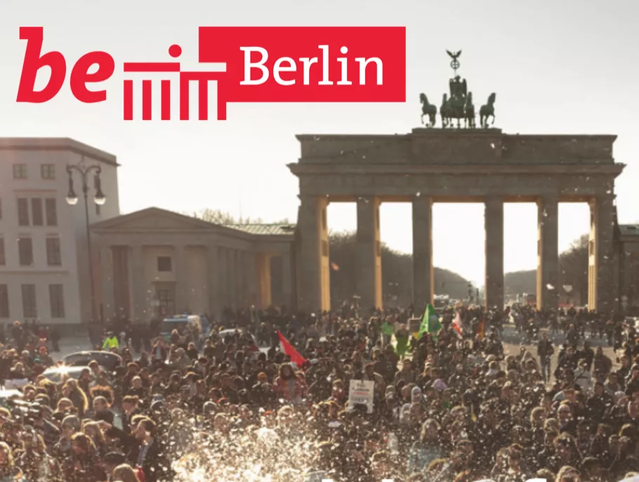 Das be Berlin Logo zusammen mit einem Foto des Brandenburger Tors gefüllt mit vielen Menschen. 