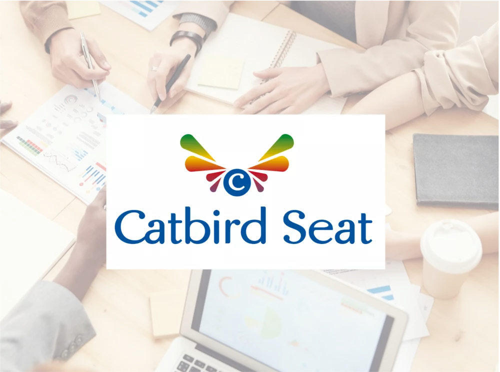 Das Catbird Seat Logo vor dem Hintergrundbild eines Büro Arbeitsplatzes. 