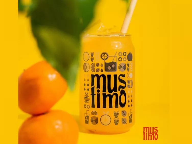 Ein Werbebild von Mustimo zeigt ein gefülltes Glas mit mustimo Aufschrift, daneben Mandarinen.